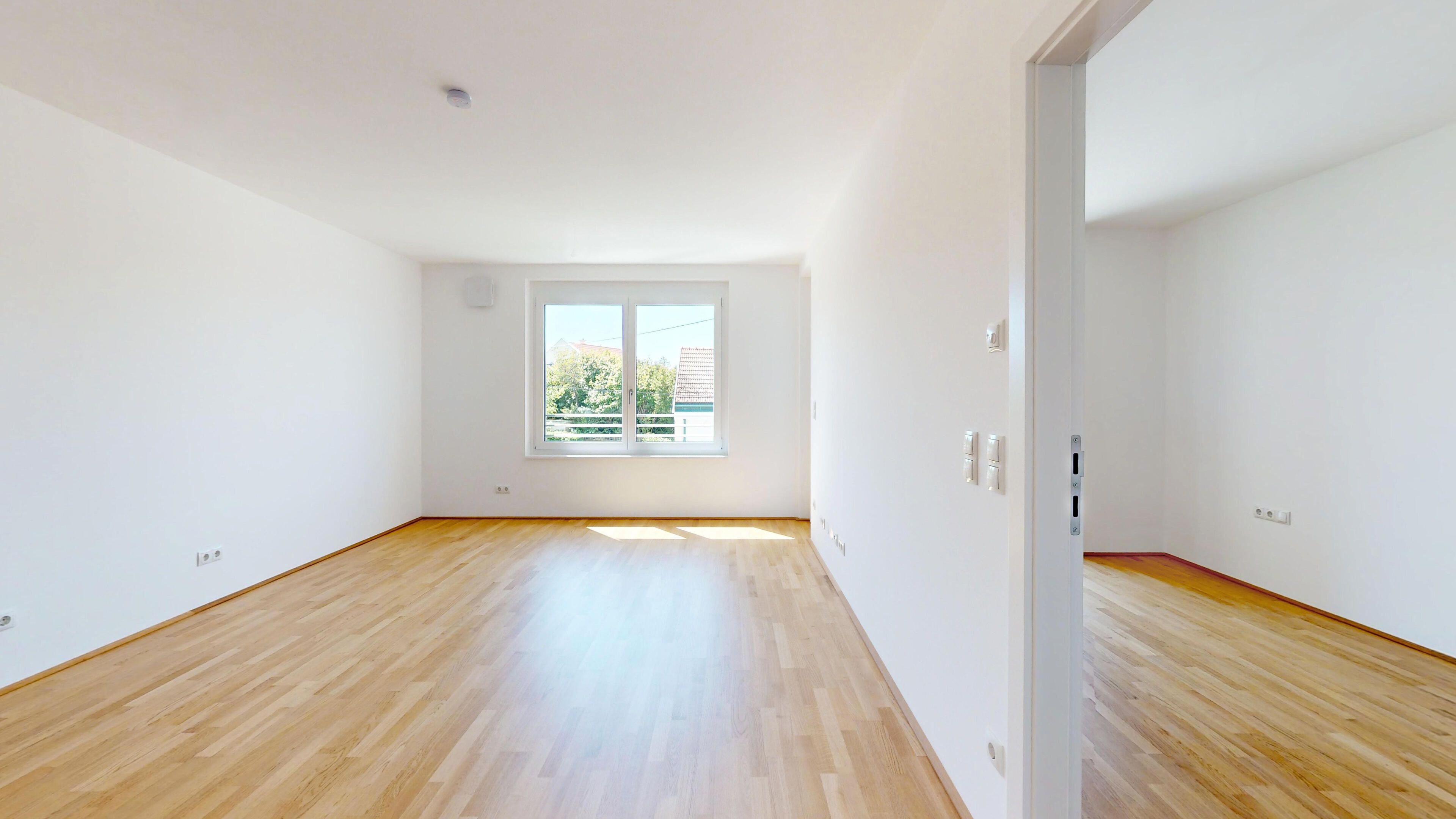 Ansicht eines geräumigen Wohnraumes mit hellem Parkettboden und Blick in den Schlafraum