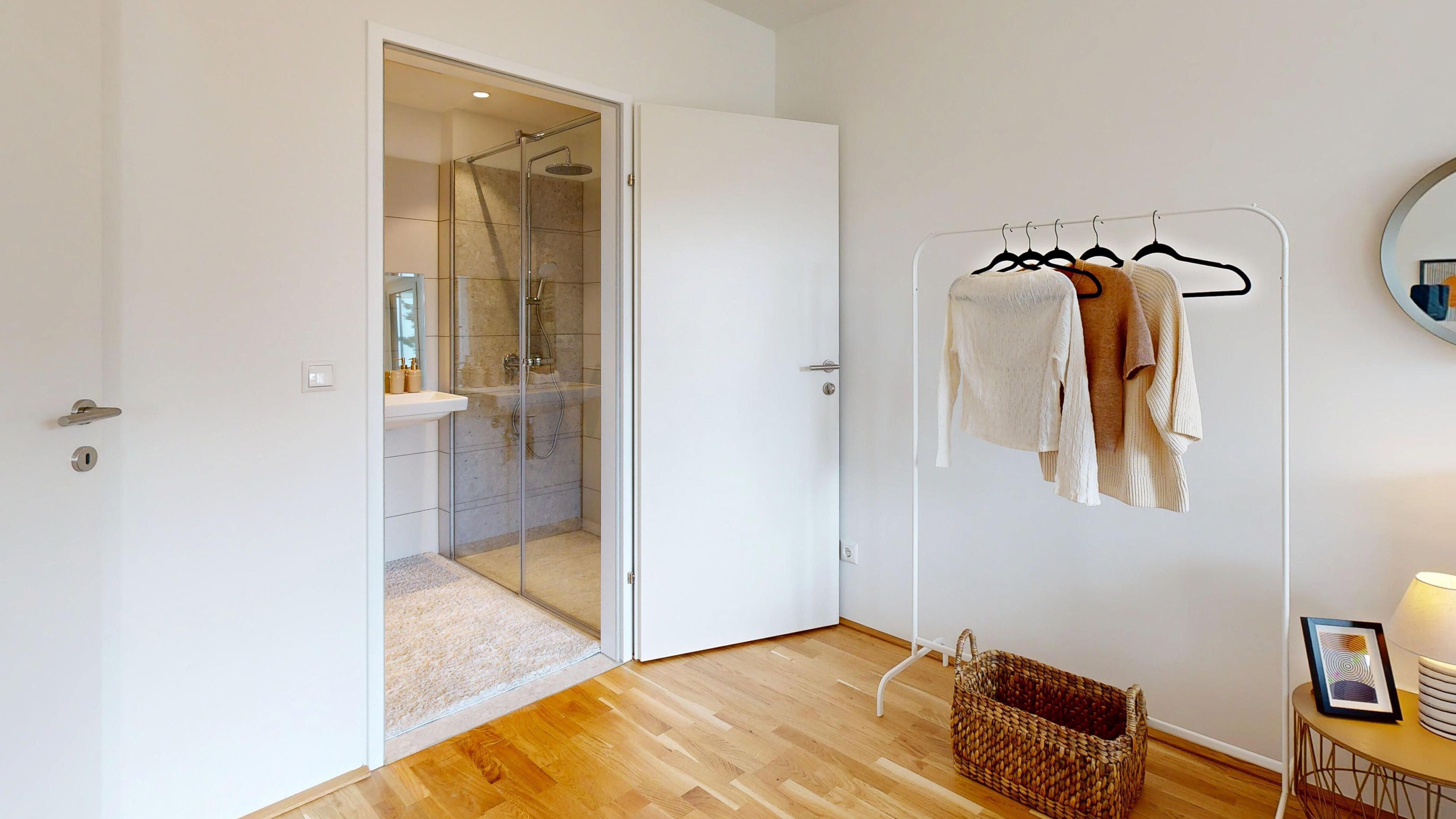 Darstellung eines Kleiderständers mit offener Innentür zum angrenzenden Badezimmer mit Dusche