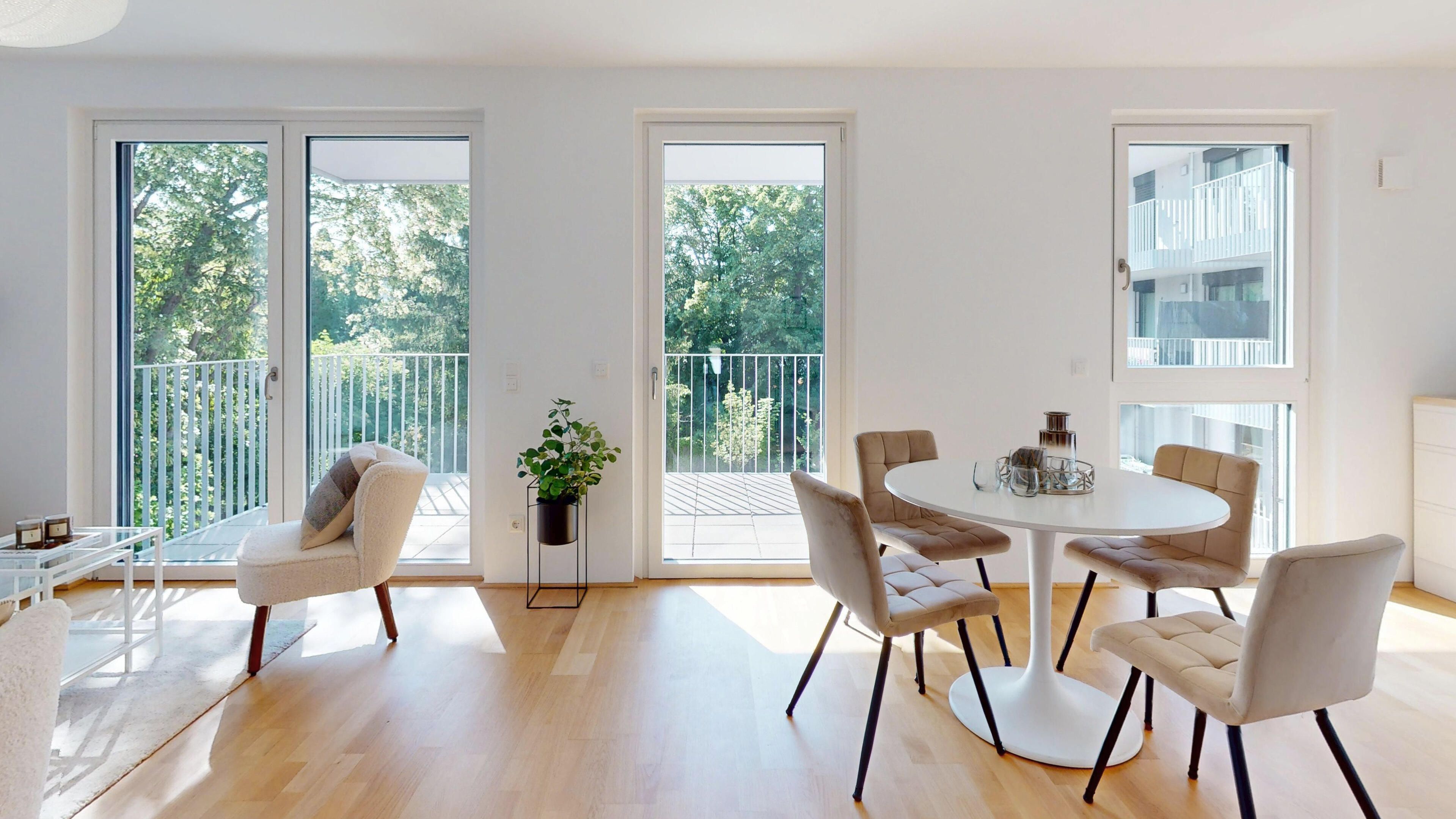 Ansicht des lichtdurchfluteten Wohnzimmers mit Esstisch und Sitzgelegenheit sowie Aussicht in den Altbaumbestand