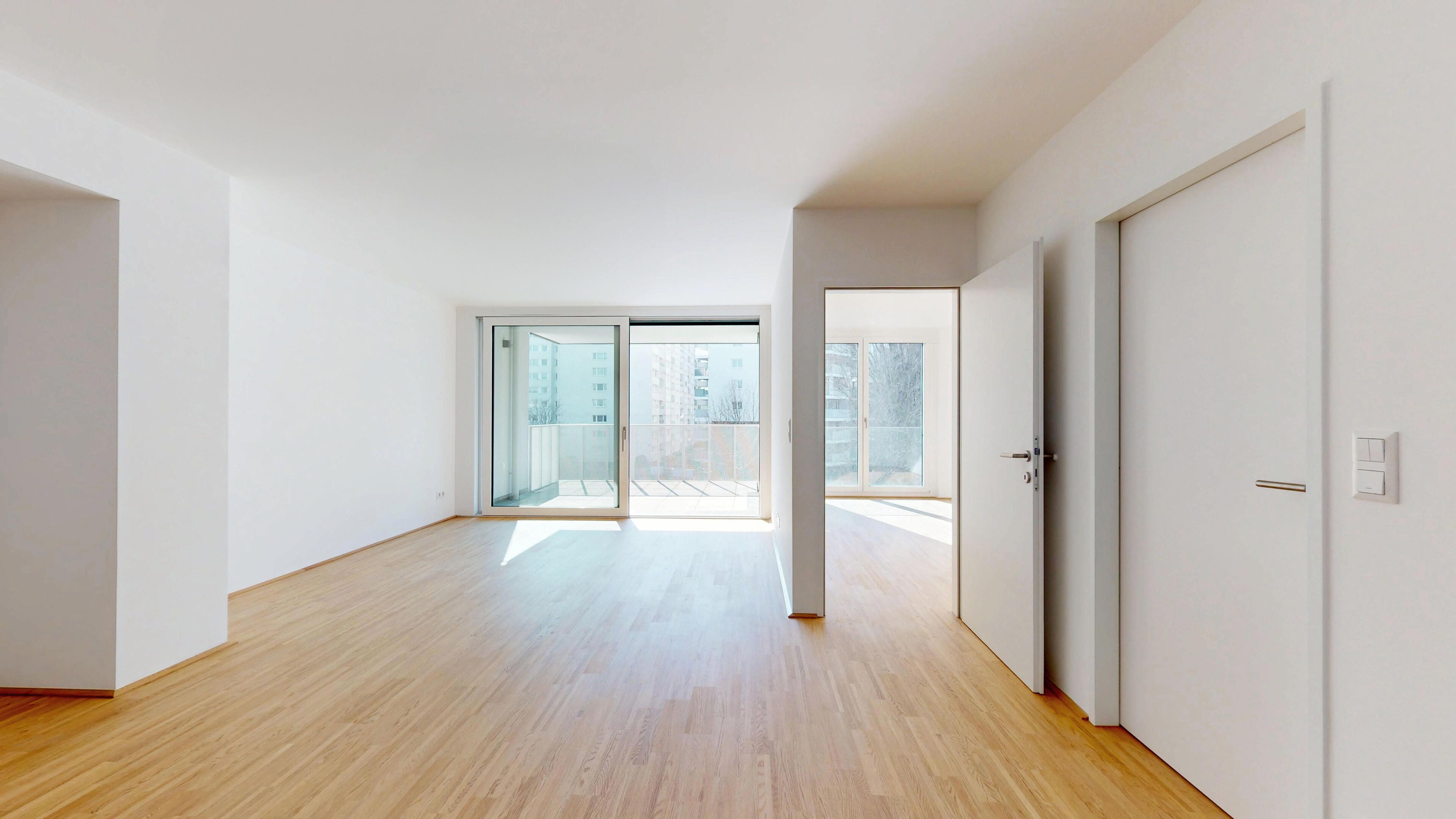 Ansicht eines geräumigen Wohnraums mit Zugang zum Balkon und Blick ins Schlafzimmer