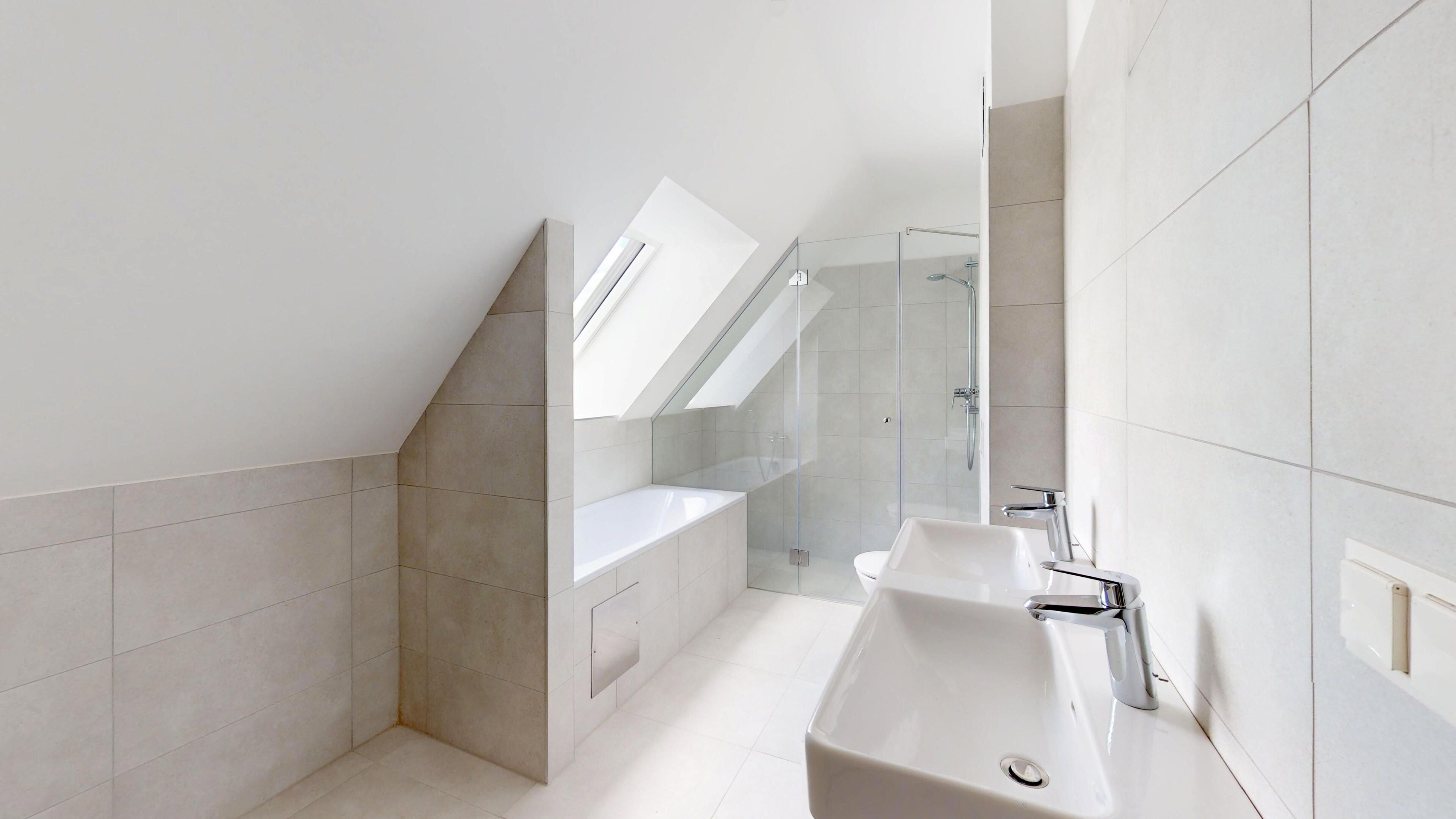 Ansicht eines sehr hellen Badezimmers mit Handwaschbecken, Dusche und Badewanne inkl. Dachflächenfenster.