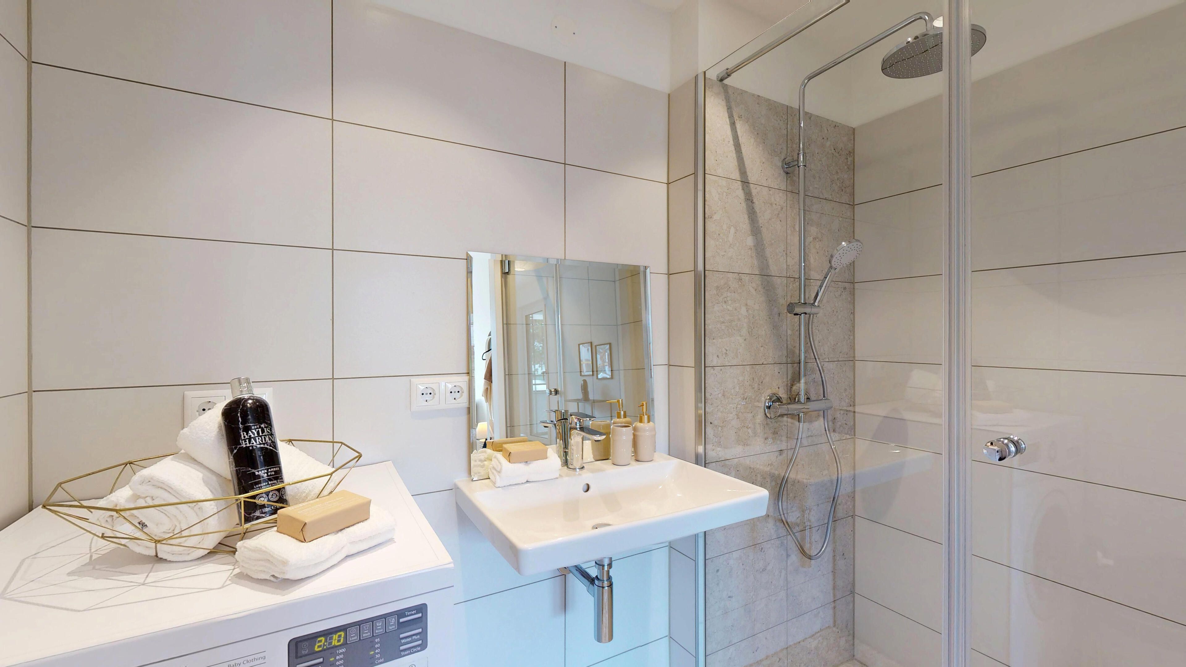 Ansicht Badezimmer mit Handwaschbecken, Dusche und Darstellung einer Waschmaschine