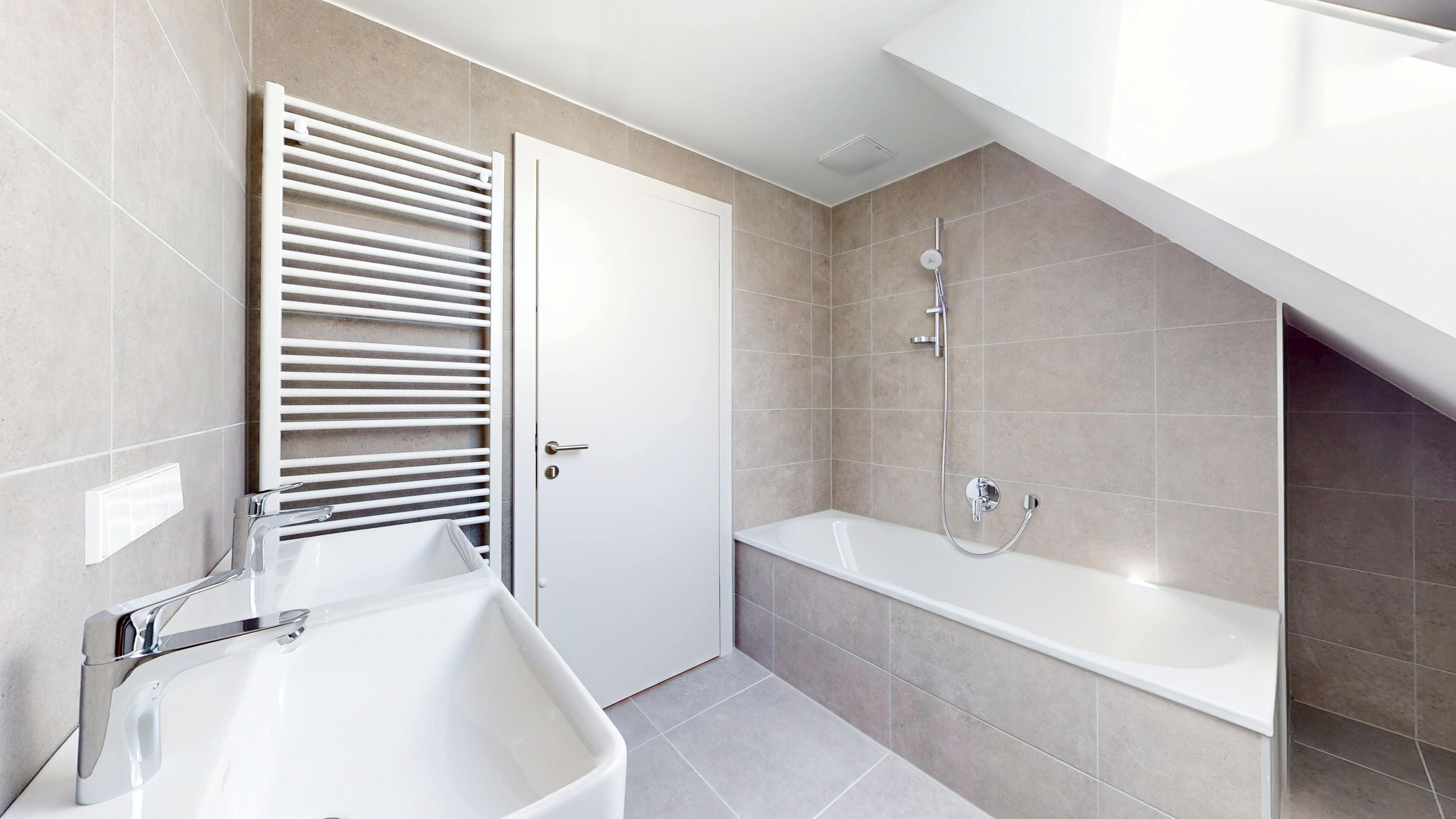 Ansicht eines Badezimmers mit Badewanne, Zimmertür, Handtuchtrockner und Handwaschbecken