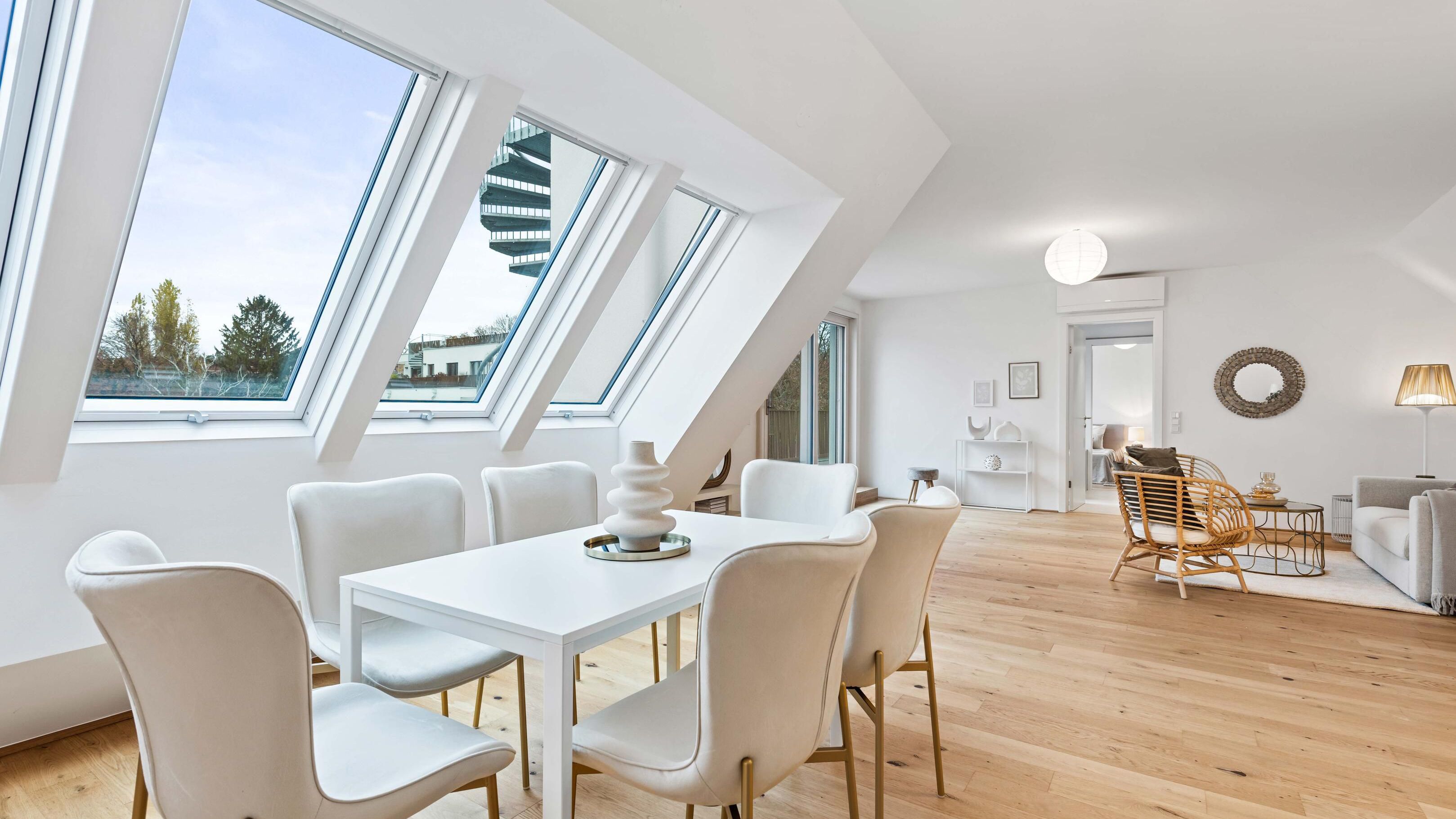 Ansicht eines hellen Wohnraums mit Dachschräge, Fensterfront und Zugang zur Terrasse. Der Wohnraum ist mit Mustermöbel dargestellt.